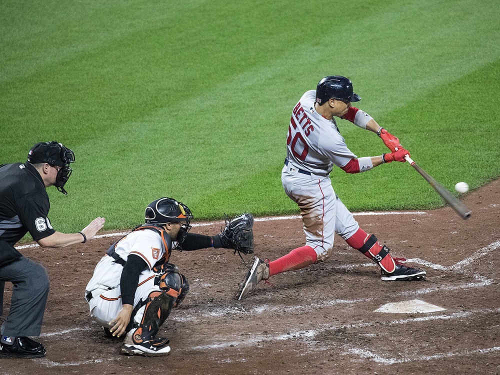 Boston Red Sox player Mookie Betts hits a pitch by swinging his bat